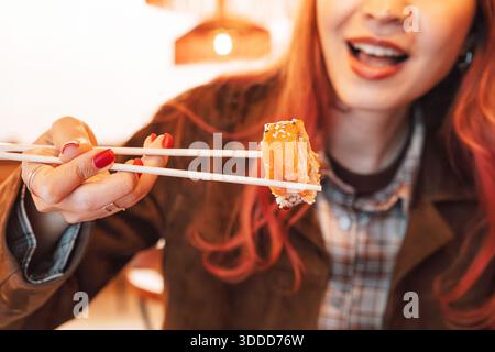 Eine junge Frau isst gerne ein köstliches Sushi-Brötchen mit Essstäbchen in einem Restaurant Stockfoto