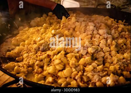 Winterliches Essen und Weinfest, nachts auf der Straße in einer riesigen Pfanne Tartiflette aus Savoyen in den französischen Alpen, zubereitet mit Kartoffeln und Reblochon Chee Stockfoto