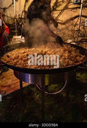 Winterliches Essen und Weinfest, nachts auf der Straße in einer riesigen Pfanne Tartiflette aus Savoyen in den französischen Alpen, zubereitet mit Kartoffeln und Reblochon Chee Stockfoto