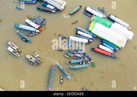 Aus der Vogelperspektive ist eine lebhafte Ansammlung von Booten auf dem schwimmenden Markt Cai Rang in Can Tho, Mekong Delta, Südvietnam zu sehen. Die Szene zeigt eine Mischung aus überdachten und offenen Schiffen, die sich um Gebäude am Fluss gruppieren, mit lebendigen Waren, die auf den Decks zu sehen sind. Stockfoto