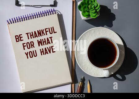 Seien Sie dankbar für das, was Sie haben Text auf Papierkarte mit Wecker und stationär auf hölzernem Hintergrund Stockfoto