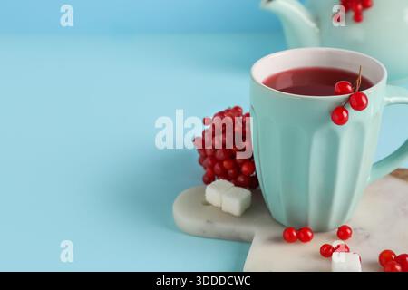 Tasse heißer Viburnum-Tee mit Beeren und Zuckerwürfeln auf blauem Hintergrund Stockfoto