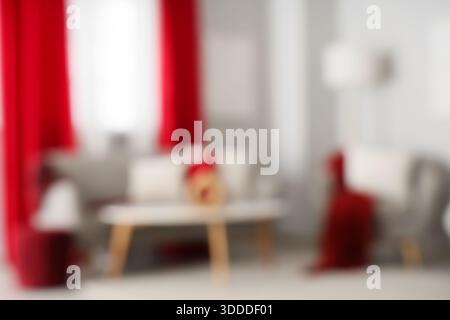 Stilvolles graues Sofa mit weichen Kissen und komfortablem Sessel neben roten Vorhängen im Wohnzimmer, verschwommener Blick Stockfoto