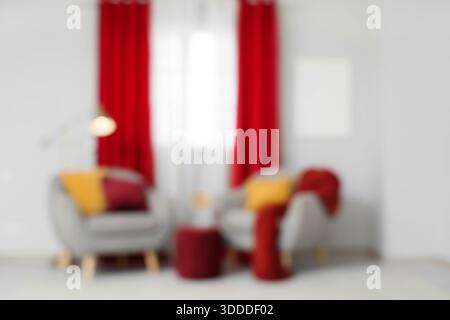 Bequeme graue Sessel mit weichen Kissen neben roten Vorhängen im Wohnzimmer, verschwommener Blick Stockfoto