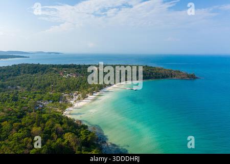 Türkisfarbenes Wasser trifft auf eine weiße Sandküste entlang einer üppigen, bewaldeten Halbinsel am Coconut Beach. Die Szene zeigt einen hölzernen Pier, verstreute kleine Gebäude und eine lebhafte tropische Vegetation unter einem hellblauen Himmel. Stockfoto