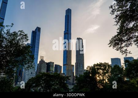 Die beeindruckende Skyline von Midtown Manhattan mit modernen Glastürmen und dem Essex House-Schild ragt in der Abenddämmerung hinter Silhouetten von Parkbäumen hervor. Stockfoto