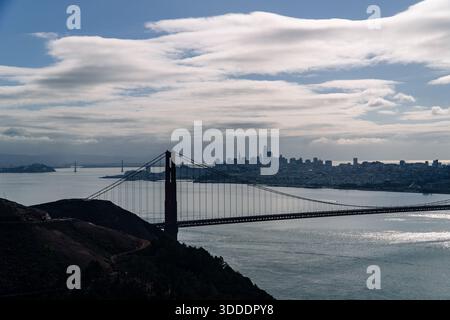 Die Golden Gate Bridge ist von einem bewölkten Himmel umgeben und die Skyline der Stadt San Francisco in der Ferne, die sich über die Bucht erstreckt. Stockfoto