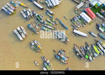 Direkte Sicht von oben zeigt eine dichte Anordnung von produktbeladenen Booten auf dem schwimmenden Markt Cai Rang in Can Tho, Mekong Delta, Südvietnam. Das Bild zeigt farbenfrohe Planen, überdachte Schiffe und Gebäude am Fluss entlang des schlammigen Flusses. Stockfoto