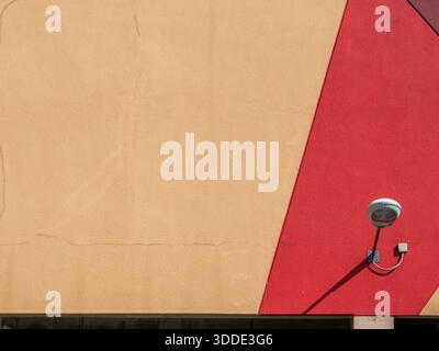 Gelb und rot lackierte Wand eines Gebäudes außen mit einer Außenbeleuchtung an der Wand. Stockfoto