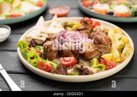 Gegrillte Hähnchenschaschlik-Stücke, serviert auf einem Teller mit gebackener Kartoffel, Lavash, Sulguni-Käse und eingelegter Zwiebeln Stockfoto