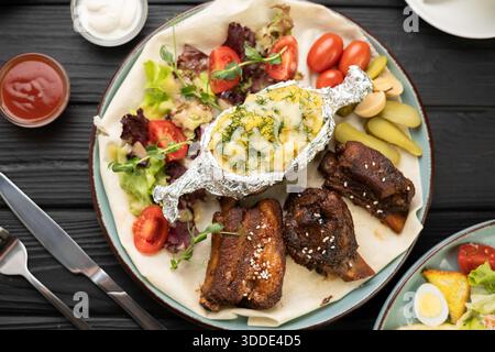 Saftige gegrillte Schweinerippchen mit gebackenen Kartoffeln, Gemüse und Tomatenketchup auf Teller im Restaurant Stockfoto