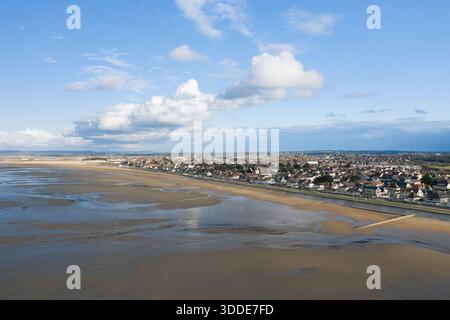 Blick aus einem hohen Winkel auf den Sword Beach in Ouistreham, mit weitläufigen sandigen Gezeitenflächen, die unter hellem Himmel mit verstreuten Wolken auf die Küstenstadt treffen. Die Szene fängt den Schnittpunkt von Natur und Architektur am Meer ein. Stockfoto