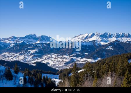 Riesige Berglandschaft mit schneebedeckten Gipfeln, bewaldeten Hängen und einem sonnigen Tal nahe Megeve unter einem leuchtend blauen Himmel. Stockfoto
