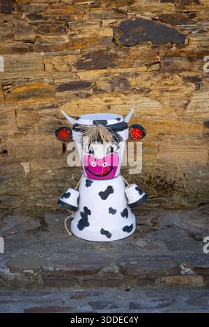 Skurrile, handgefertigte Kuhfigur aus bemalten Terrakottatöpfen mit Strohhaaren, stehend an einer rustikalen Steinmauer, vertikal Stockfoto