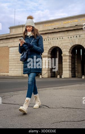 Junge kaukasische Frau, die im Winter durch das äußere Schlosstor Wien geht Stockfoto