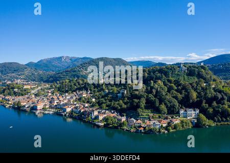 Aus der Vogelperspektive von Orta San Giulio, eingebettet am Ufer des Orta-Sees in Norditalien, mit üppigen bewaldeten Hügeln, die sich hinter der Stadt am See erheben. Die Szene bietet klares blaues Wasser, verstreute Villen und einen lebendigen Himmel, der eine ruhige Landschaft schafft. Stockfoto