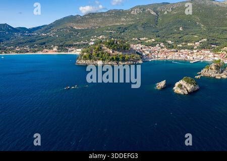 Weite Aussicht aus der Vogelperspektive auf die historische Festung auf einem Hügel, umgeben von Kiefern über der türkisfarbenen Bucht und den farbenfrohen Häusern von Parga in Epirus, Griechenland. Die mediterrane Szene bietet felsige Inselchen, tiefblaues Wasser und bewaldete Berge unter klarem Himmel. Stockfoto