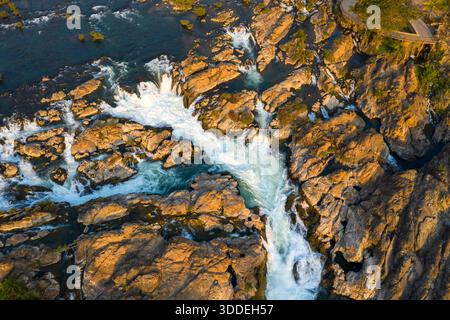 Die Aussicht über den Himmel zeigt die Tat Somphamit Wasserfälle, auch bekannt als Li Phi Falls, in der Provinz Champasak im Süden von Laos. Das warme Licht bei Sonnenuntergang hebt zerklüftete Steinformationen, energische Kaskaden und wirbelndes Wasser zwischen strukturierten Felsen hervor. Stockfoto