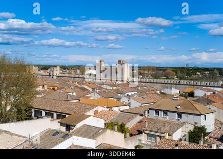 Panoramablick auf Aigues-Mortes mit sonnenbeleuchteten Ziegeldächern und den imposanten mittelalterlichen Stadtmauern unter einem leuchtend blauen Himmel mit verstreuten Wolken. Stockfoto