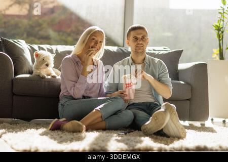 Ein Paar sitzt auf einem Teppich und genießt Popcorn zu Hause Stockfoto