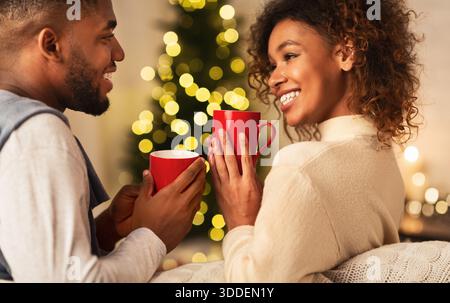 Das liebende afroamerikanische Paar trinkt Tee gegen den Weihnachtsbaum Stockfoto