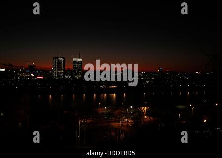 Die Lichter der Stadt Belgrad leuchten entlang des Flusses, während rote Sonnenuntergänge vom Winterhimmel verschwinden. Belgrad, Serbien - 30. Dezember 2025. Stockfoto