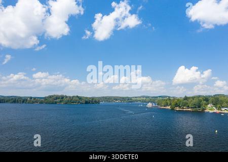 Weitläufiger Blick über den Lac des Settons mit tiefblauem Wasser, verstreuten Segelbooten und einer bewaldeten Küste unter einem hellen Himmel voller flauschiger weißer Wolken. Stockfoto