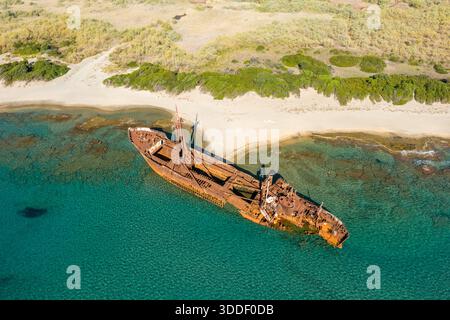 Drohnenperspektive auf das verrostete Dimitrios-Schiffswrack, das in klarem türkisfarbenem Wasser an einer Sandküste nahe Gythio ruht, umgeben von wilder Vegetation und sonnendurchfluteten Küstenstrukturen. Stockfoto