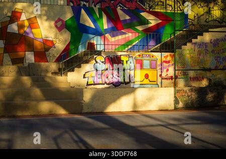Sonniger Blick auf eine farbenfrohe Treppe im Viertel Santa Teresa, Rio de Janeiro, mit geometrischen Graffiti und dem berühmten gelben Straßenbahngemälde. Stockfoto