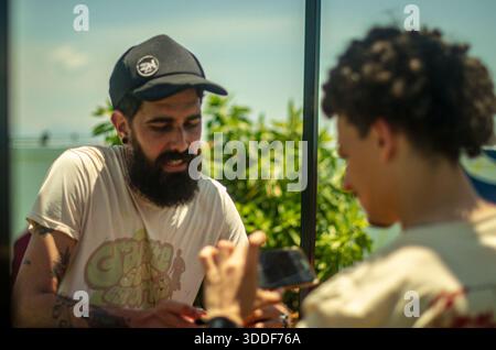 Offene mittlere Aufnahme von zwei jungen Männern, die tagsüber Inhalte auf einem Smartphone in einer urbanen Umgebung diskutieren. Stockfoto
