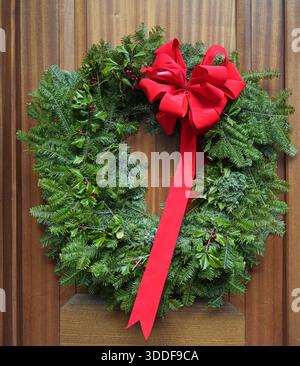 Dekorativer Weihnachtskranz aus natürlichen Evergeen-Zweigen an Holzmasertür Stockfoto