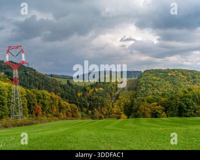 Herbstliche Berglandschaft mit Strommasten und Wald. Gemähte Wiese im Vordergrund. Bewölkter Himmel mit grauen Wolken. Vrsatec, Slowakei Stockfoto