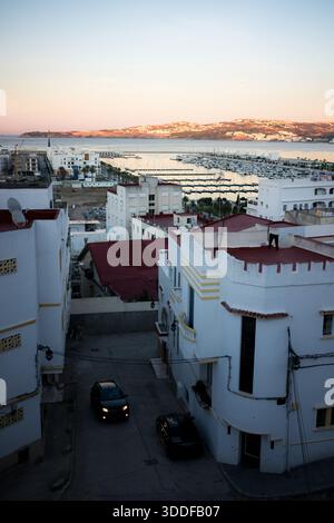 Abendblick über die Dächer von Tanger in Richtung Yachthafen und Straße von Gibraltar, mit weißen Häusern, ruhigen Straßen und sanftem Sonnenuntergang über der Bucht Stockfoto