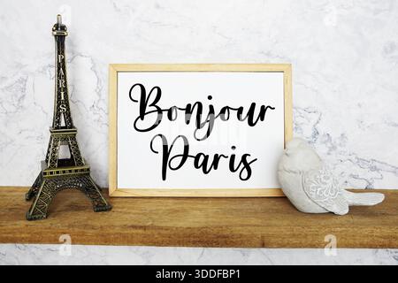 Bonjour Paris Text auf Whiteboard mit Eiffelturm Souvenir und Vogelstatue auf Holzregal Stockfoto