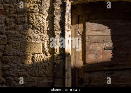 Nahaufnahme einer rustikalen Steinfassade und alter Holztür, die teilweise von warmem Sonnenlicht in Nevers beleuchtet wird. Das Bild hebt raue Texturen, natürliche Schatten und den veralteten Charakter traditioneller urbaner Architektur hervor. Stockfoto
