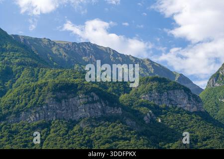 Grüne Hänge mit freiliegenden felsigen Klippen erheben sich scharf unter einem blauen Himmel mit Wolken im Massif des Bauges in den französischen Alpen. Stockfoto