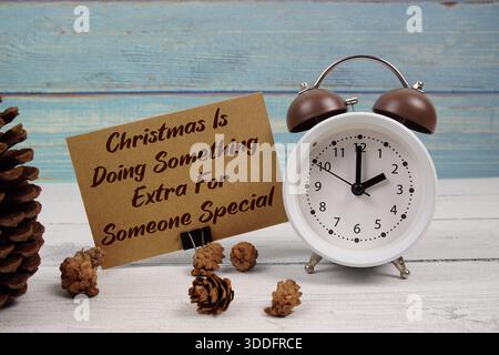 Weihnachten macht etwas Besonderes für jemanden spezieller Text auf Papierkarte mit Wecker und Tannenzapfen Dekoration auf hölzernem Hintergrund Stockfoto