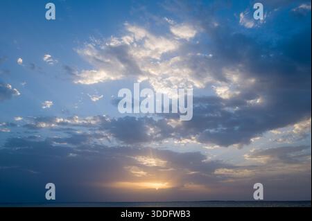 Dramatischer Sonnenuntergang über dem Mittelmeer in der Nähe von Oristano, Sardinien, mit Sonnenstrahlen, die in Schichten durchdringen, und sanftem goldenem Licht, das auf ruhigem Wasser reflektiert. Der weitläufige Himmel erzeugt eine friedliche, luftige Stimmung. Stockfoto