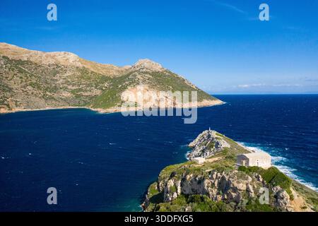 Blick aus der Vogelperspektive auf eine kleine weiße Kapelle auf einem felsigen Vorsprung, umgeben von tiefblauem Meer, mit zerklüfteten Hügeln und klarem Himmel in Porto Kagio, Griechenland. Stockfoto