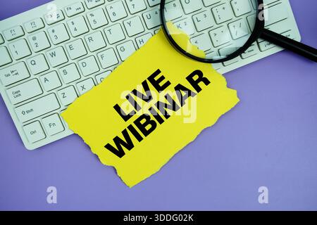 Gelbes Papier mit Text „Live Webinar“ und Lupe auf einer weißen Tastatur Stockfoto