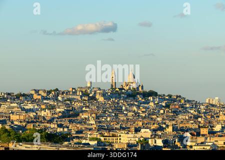 Ein Panoramablick auf Montmartre bietet die berühmte Basilika Sacre-Cur, die sich über einem Meer aus Pariser Dächern erhebt und in sanftes goldenes Licht unter einem klaren Abendhimmel getaucht ist. Stockfoto