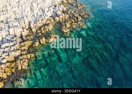 Aus der Vogelperspektive auf die sonnengebleichte felsige Küste trifft auf das türkisfarbene Meer in Magne, Griechenland. Die strukturierten Steine und das lebendige Wasser erzeugen einen beeindruckenden natürlichen Kontrast bei hellem Tageslicht. Stockfoto