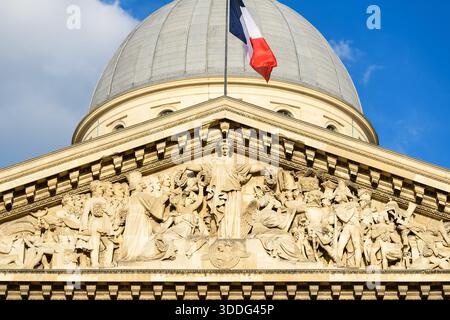 Nahaufnahme des reich verzierten Steingiebels des Pantheons mit detaillierten neoklassizistischen Reliefskulpturen unter der großen Kuppel und einer französischen Flagge, die von hellem Sonnenlicht vor einem leuchtend blauen Himmel beleuchtet wird. Stockfoto