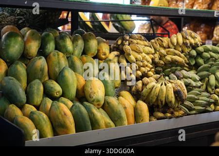 Farbenfrohe Marktpräsentation frischer Papayas in verschiedenen Reifestadien sowie reife Bananen und grüne Kochbananen, in ordentlichen Abfalleimern angeordnet. Stockfoto