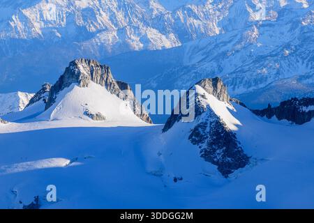 Zwei scharfe, schneebedeckte Berggipfel erheben sich über einen ausladenden Gletscher im Mont Blanc-Massiv, mit tiefblauen Schatten und klarem Winterlicht, das dramatische alpine Texturen hervorhebt. Stockfoto