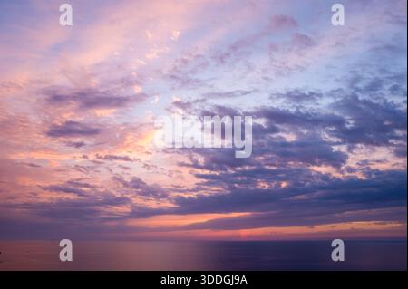 Bunte Streifen aus Lavendel, Rosa und Blau erstrecken sich über den Abendhimmel über dem ruhigen Wasser des Mittelmeers. Die ruhige Szene ist in sanftes, glühendes Dämmerungslicht getaucht und schafft eine ruhige und stimmungsvolle Stimmung. Stockfoto