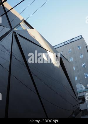 Moderne schwarze architektonische Fassade mit scharfen geometrischen Linien und Stromkabeln vor klarem blauem Himmel in Jimbocho Tokio Stockfoto