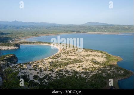 Panoramablick auf Voidokilia Beach's ikonische sichelförmige Sandbar und die ruhige blaue Lagune, umgeben von niedrigen Dünen und üppiger mediterraner Vegetation in Messenia, Peloponnes. Stockfoto