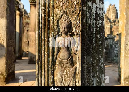 Die kunstvoll geschnitzte apsara-Figur ziert eine verwitterte Sandsteinsäule im Bayon-Tempel in Angkor, Kambodscha. Warmes Sonnenlicht unterstreicht das detaillierte Khmer-Relief und den strukturierten Stein in den antiken Ruinen. Stockfoto