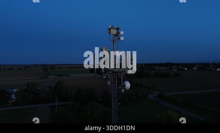 Mobilfunkturm steht vor dem dunkelblauen Himmel, ausgestattet mit verschiedenen Antennen für drahtlose Kommunikation und Mobilfunkdienste im gesamten Po Val Stockfoto